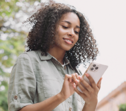 Woman outside, smiling while looking at her smartphone in her hands.